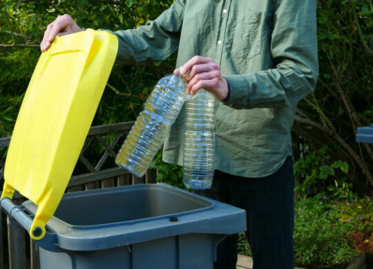 Man putting plastic bottles in a yellow bin for recycling.